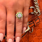 Close-up of a hand wearing a gold ring with a green gemstone against an orange textured background.