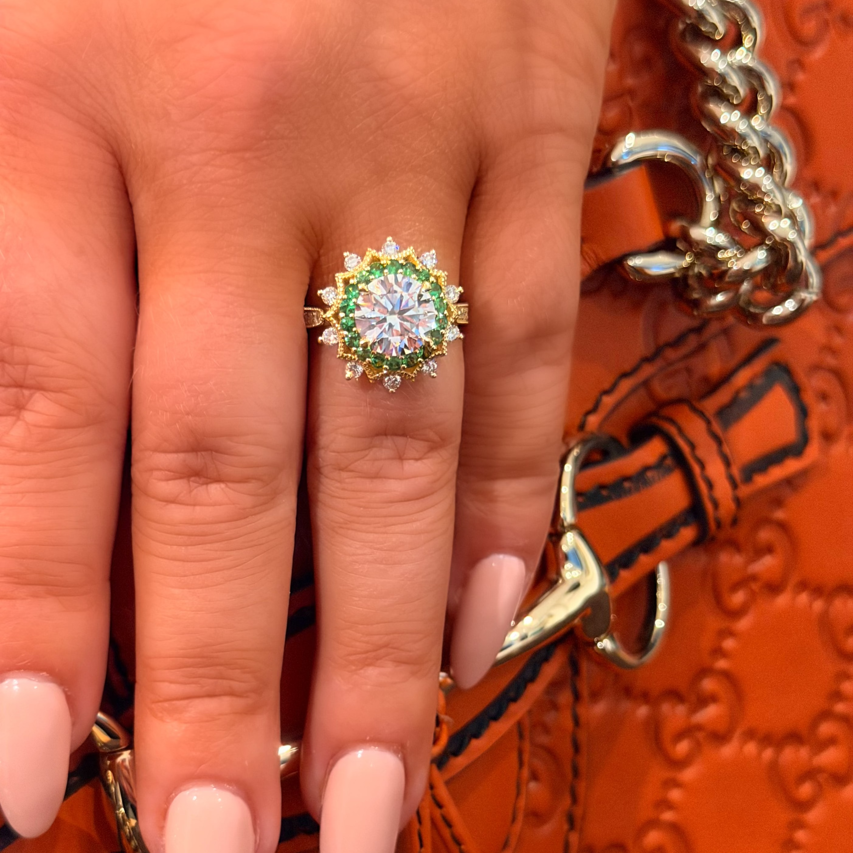 Close-up of a hand wearing a gold ring with a green gemstone against an orange textured background.