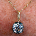 A close-up of a gold chain necklace with a cushion-cut clear gemstone pendant resting on human skin.