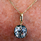 A close-up of a gold chain necklace with a cushion-cut clear gemstone pendant resting on human skin.
