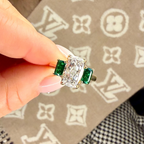Diamond and emerald ring held by a hand on a patterned surface