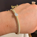 A gold snake-style bangle bracelet with a square diamond pavé center stone, shown worn on a person's wrist.