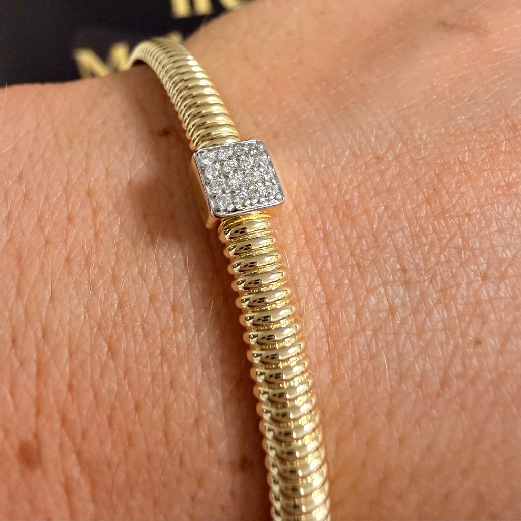A gold snake-style bracelet with a square pavé diamond charm, shown worn on a person's wrist.