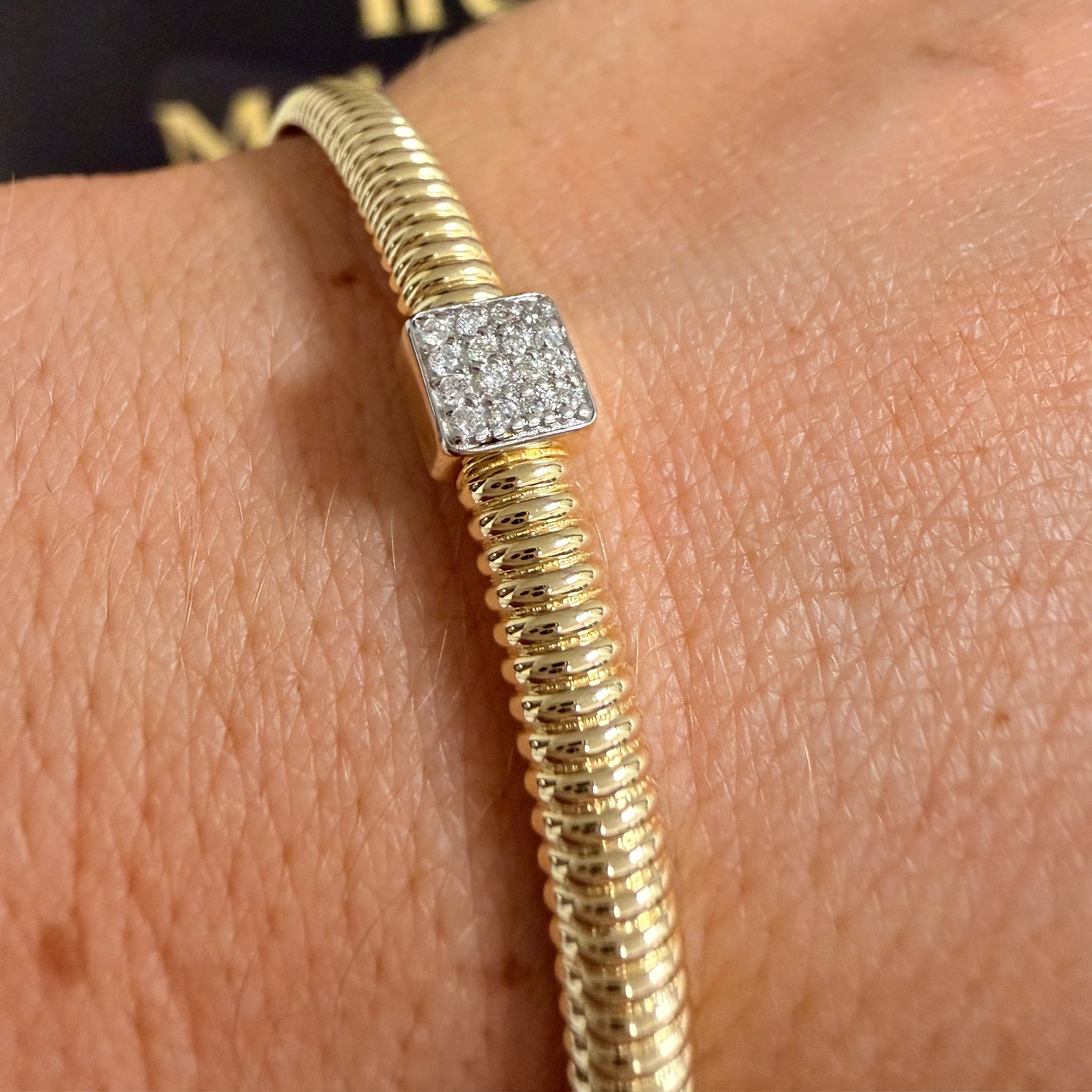 A gold snake-style bracelet with a square pavé diamond charm, shown worn on a person's wrist.
