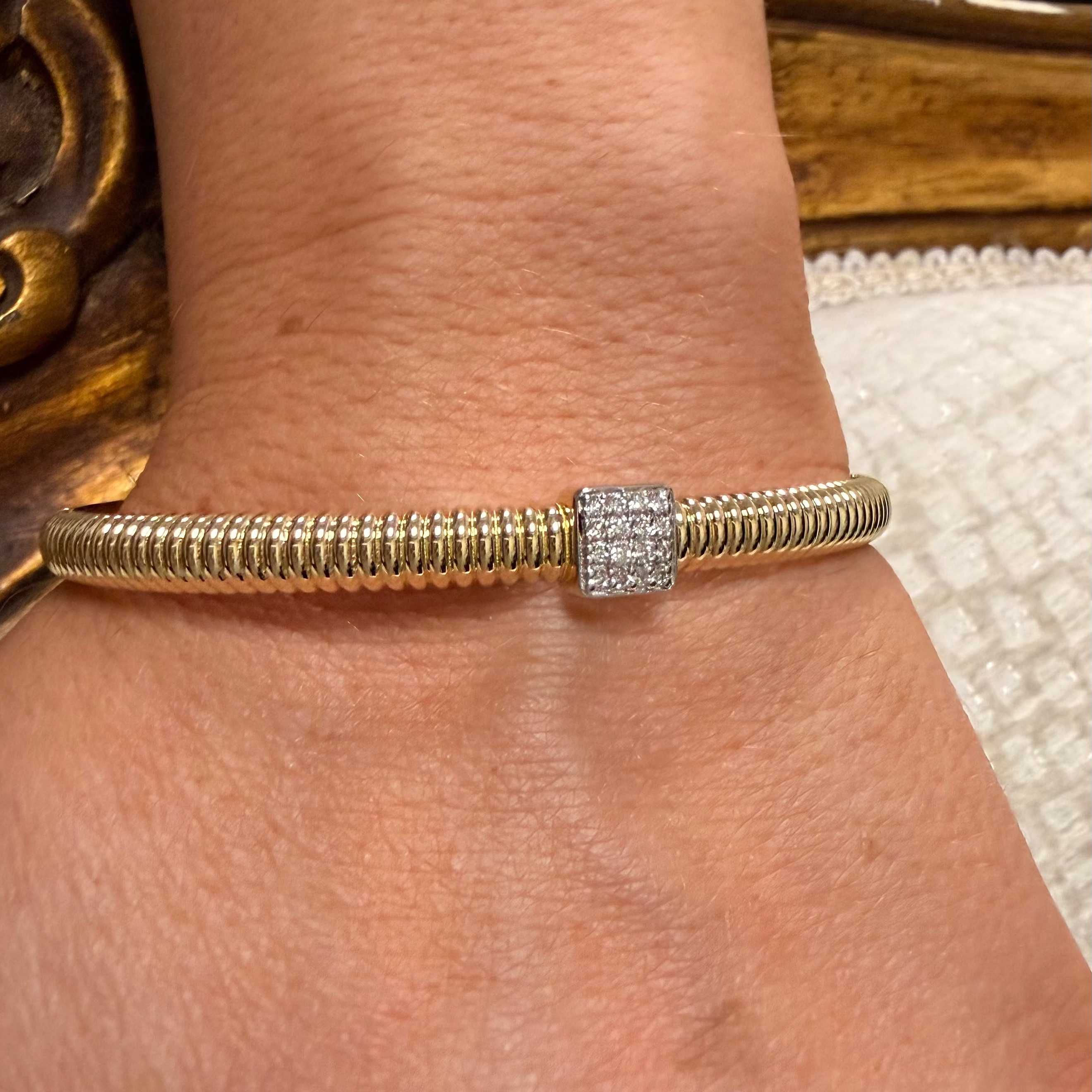 A close-up of a person's wrist wearing a gold snake-style bracelet with a square diamond cluster setting.