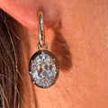 A close-up of a person's ear wearing a gold hoop earring with a round brilliant-cut clear gemstone in a bezel setting.