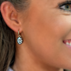 A close-up of a woman wearing a small gold hoop earring with a round clear gemstone, shown against her ear and side profile.