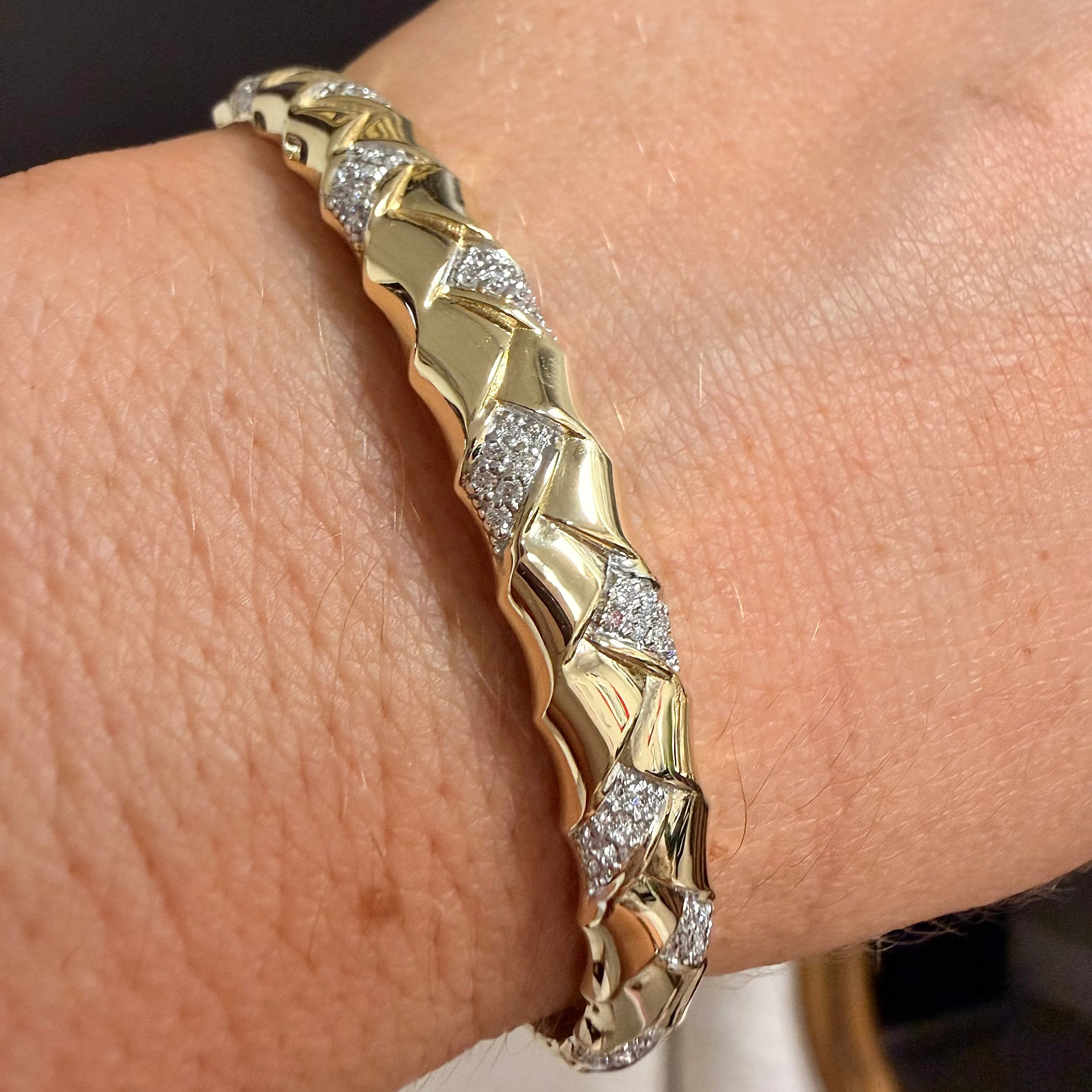 A close-up of a gold and silver-toned diamond-encrusted bangle bracelet worn on a person's wrist.