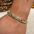 A close-up of a person's wrist wearing a gold bangle bracelet with pavé-set clear stones and a textured, segmented design.