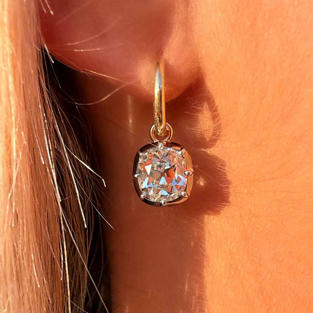 Gold earring with a large diamond on an ear against a neutral background