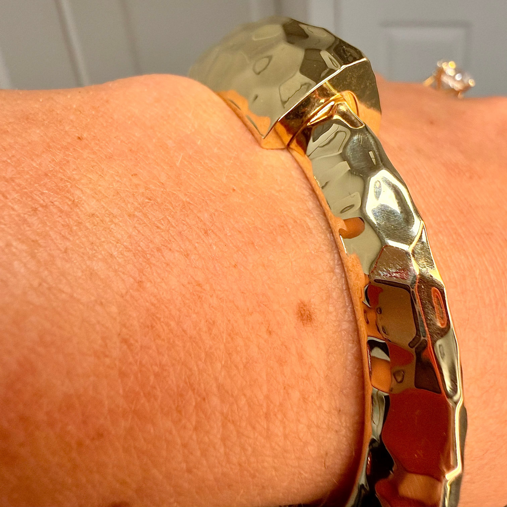Gold bracelet on a wrist with a neutral background