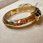Gold bracelet on a textured surface with a brand name visible