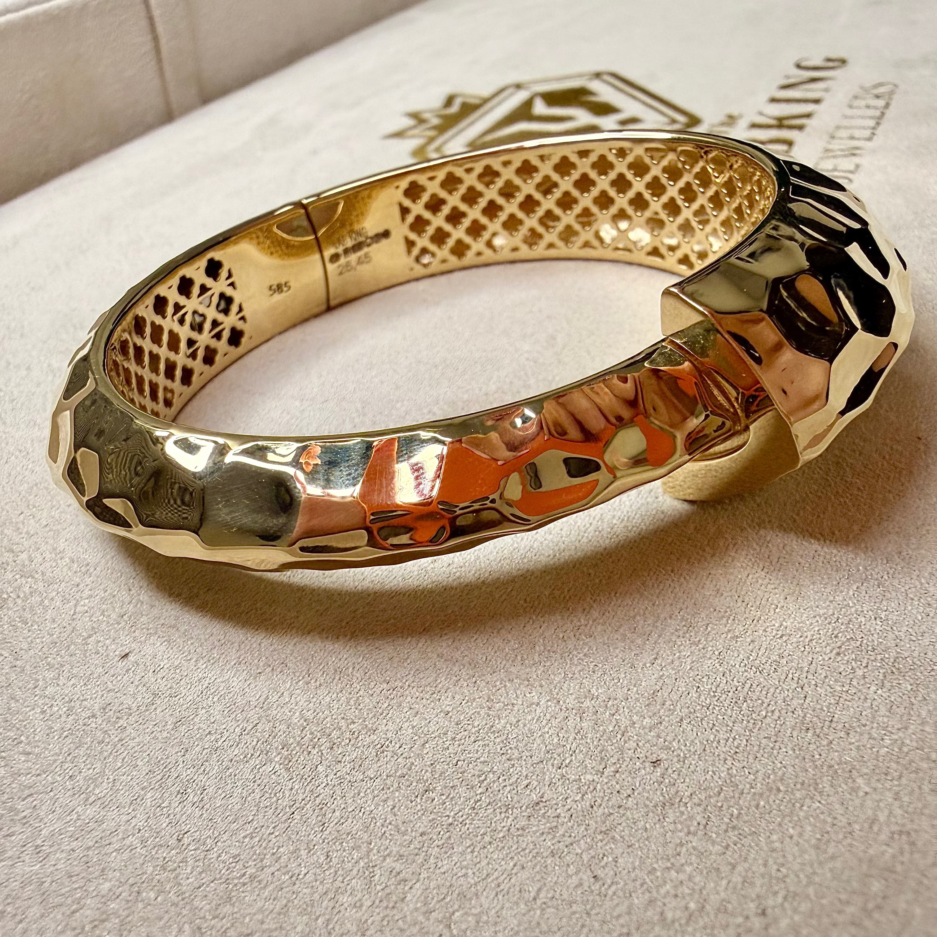 Gold bracelet on a textured surface with a brand name visible