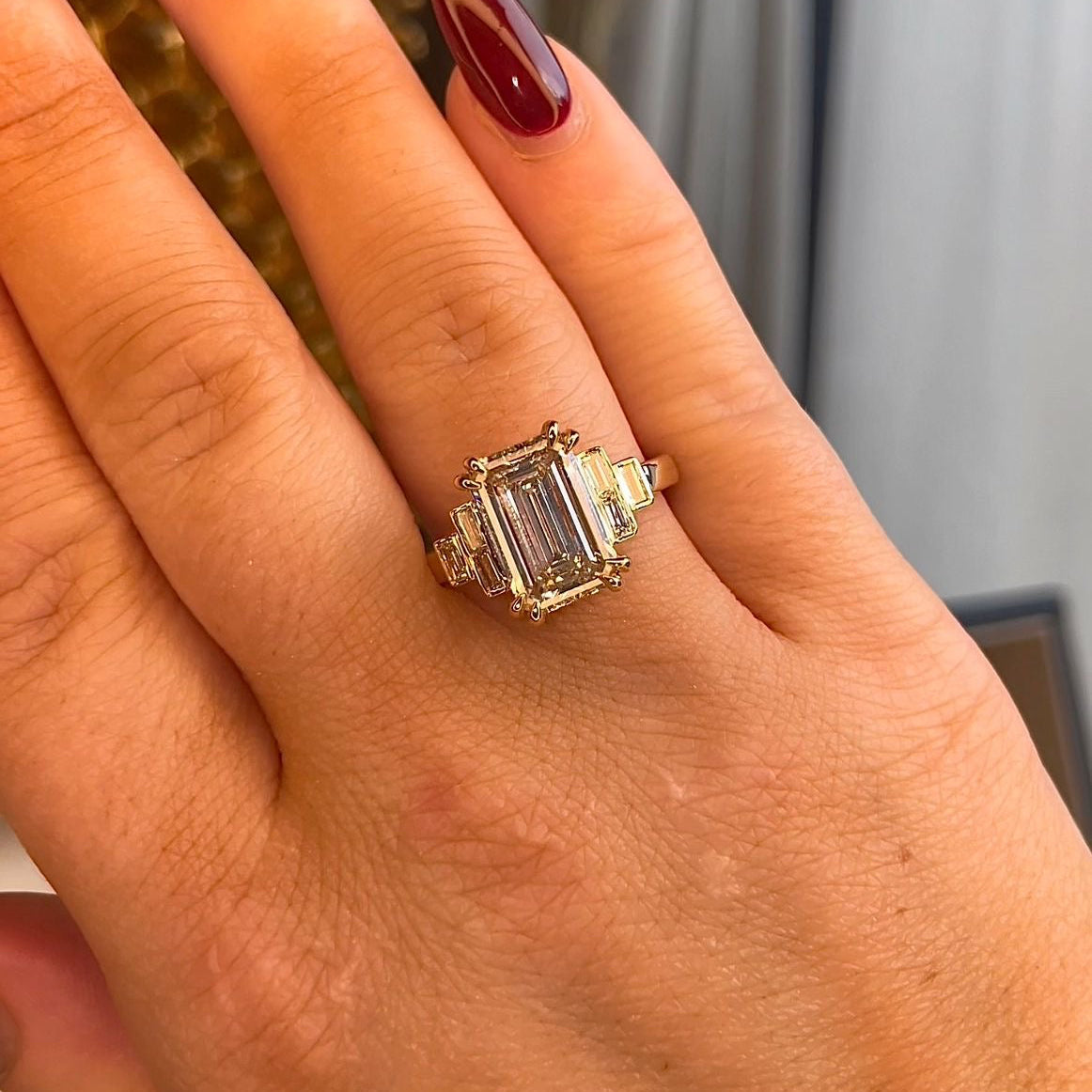 Hand wearing a ring with a large gemstone, set against a neutral background