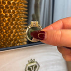 Gold ring held by a hand with red nail polish, displayed on a branded jewelry box.
