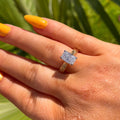Hand wearing a diamond ring with green foliage in the background