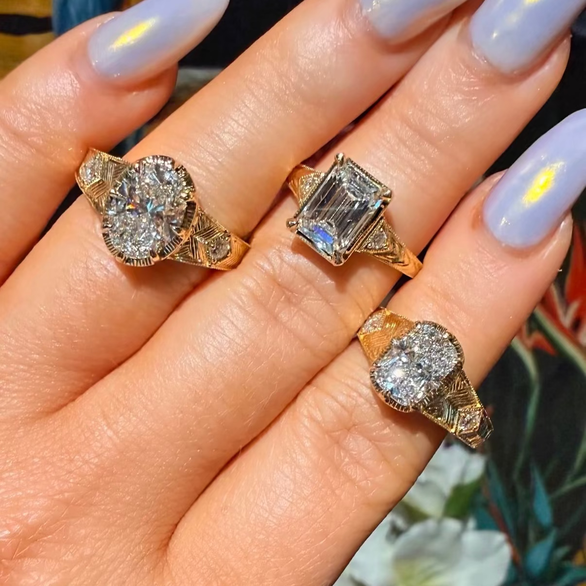 Hand wearing three diamond rings with light purple nail polish.