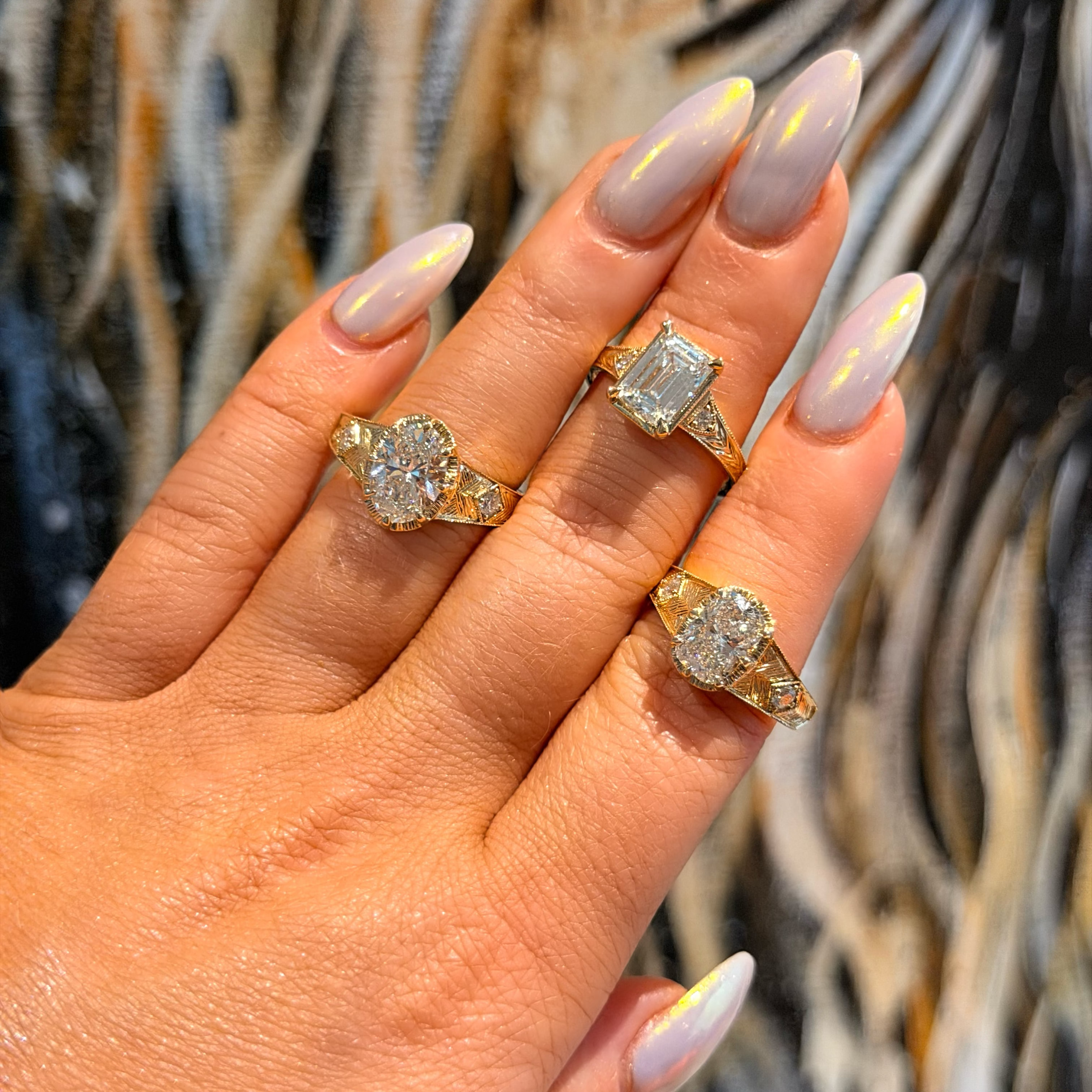 Hand wearing three diamond rings with matching nail polish against a blurred background