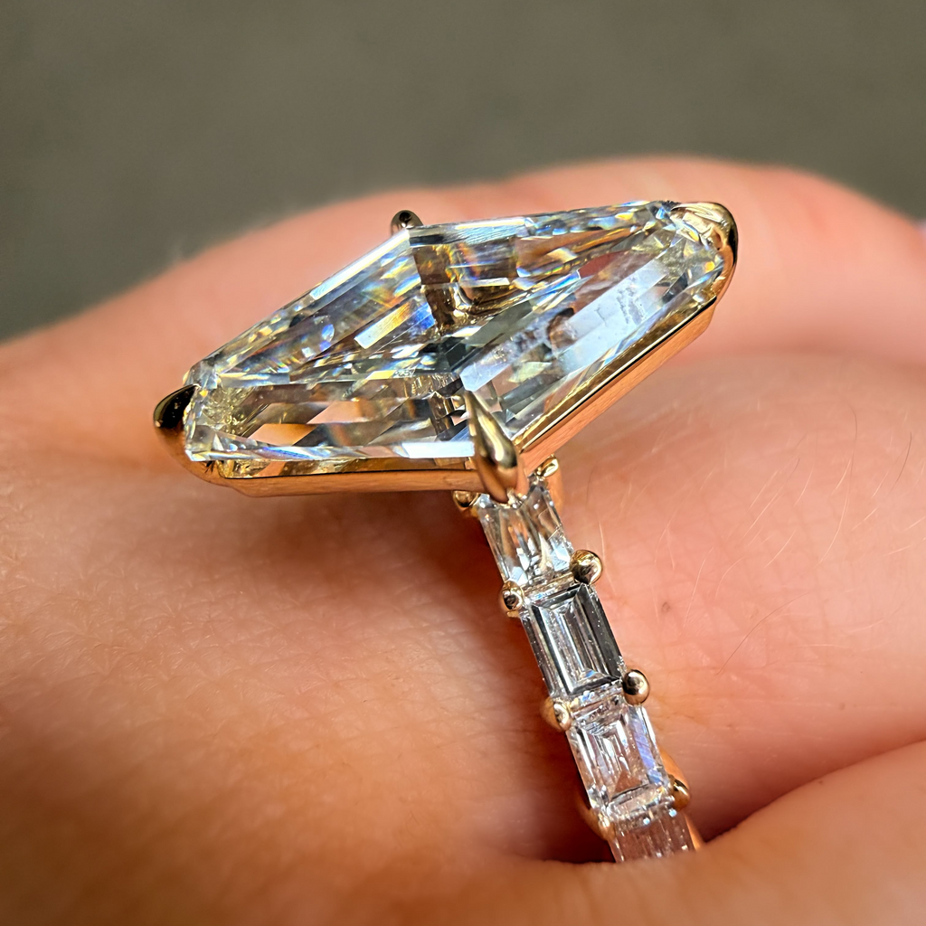 Gold ring with a large diamond and smaller baguette diamonds on a finger.
