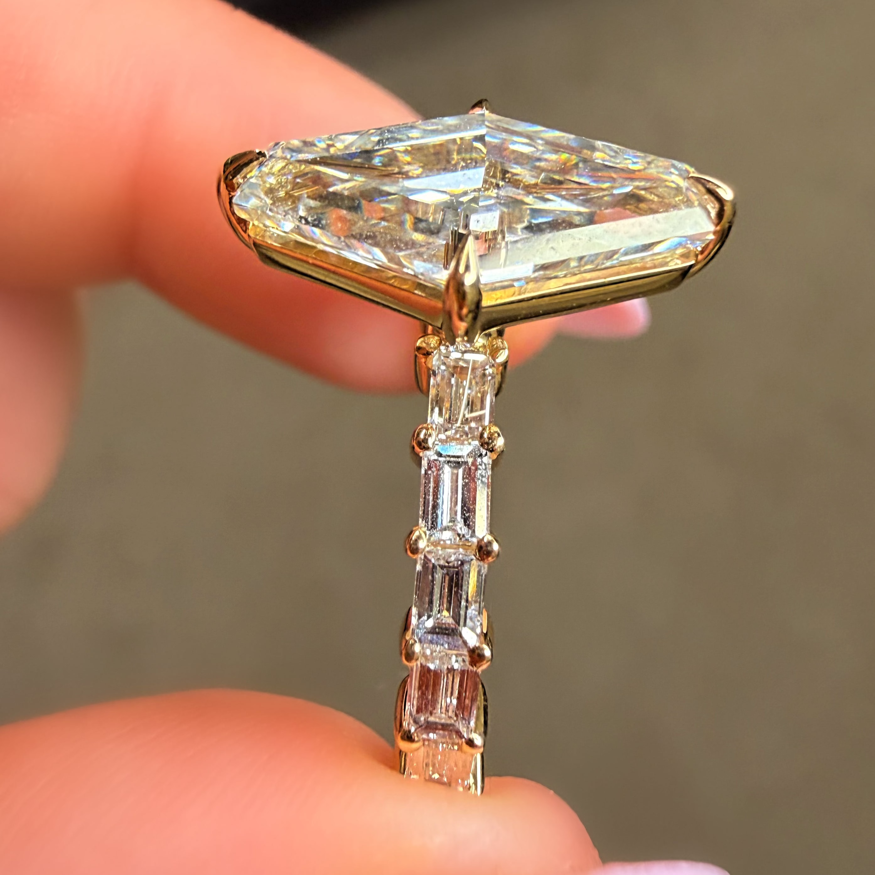 Gold ring with a large diamond and smaller baguette-cut diamonds held between fingers.