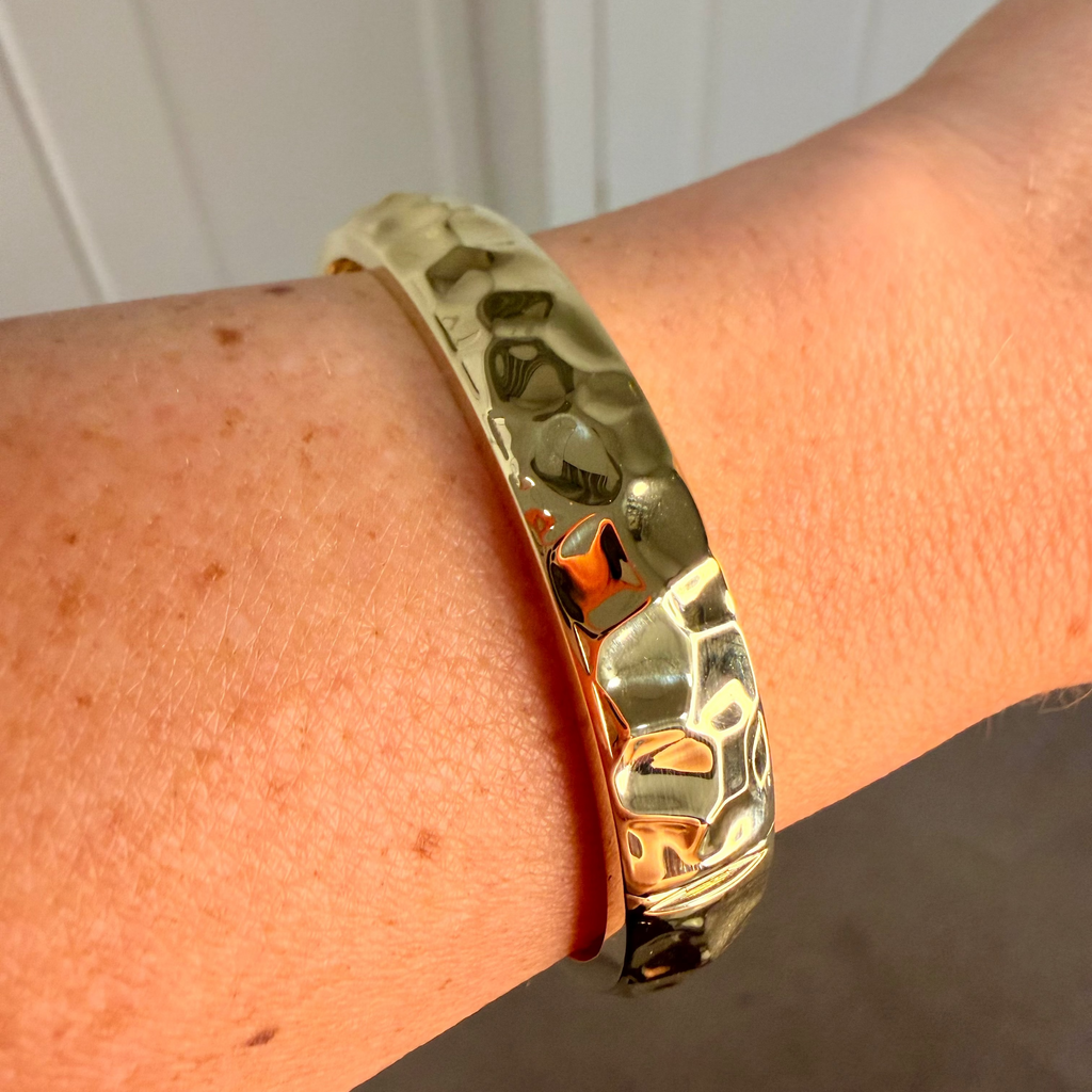 Gold bracelet on a wrist with a neutral background