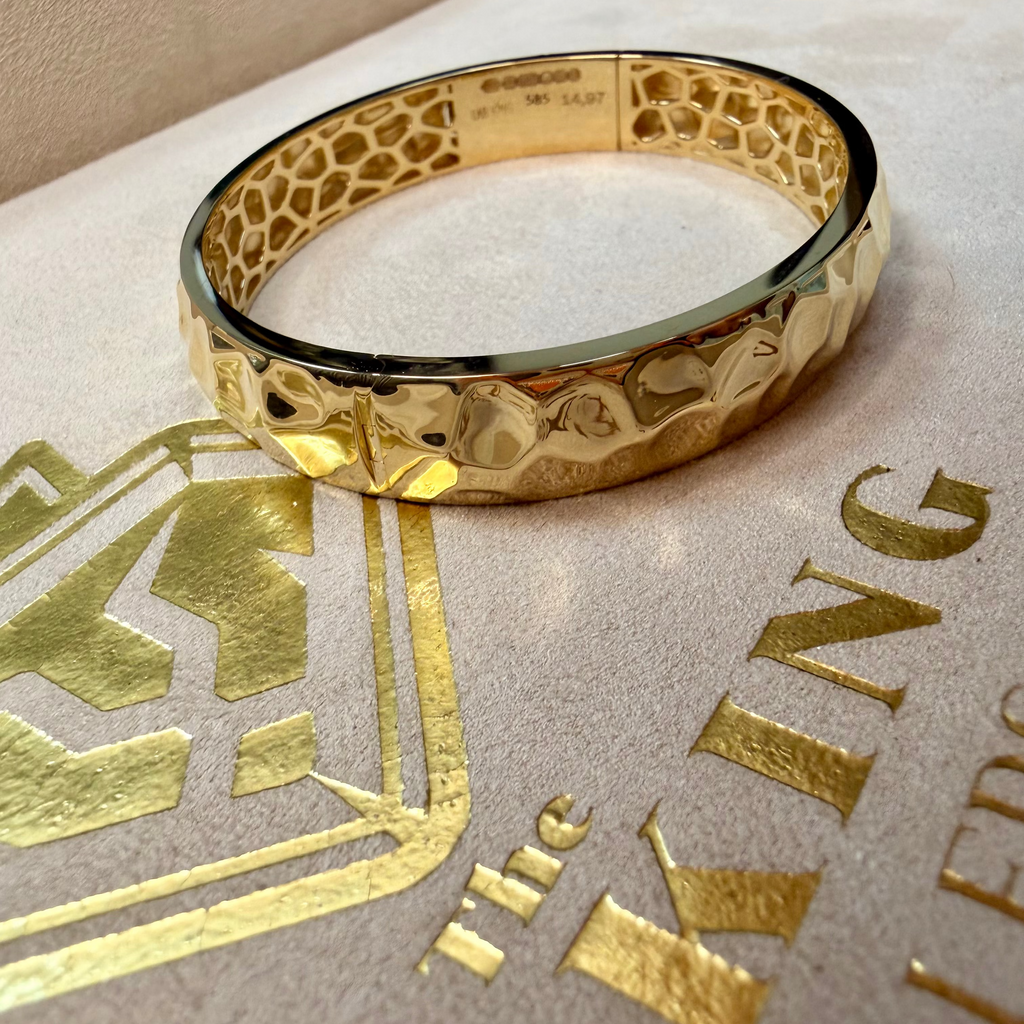 Gold bracelet on a textured surface with 'The King's' branding.