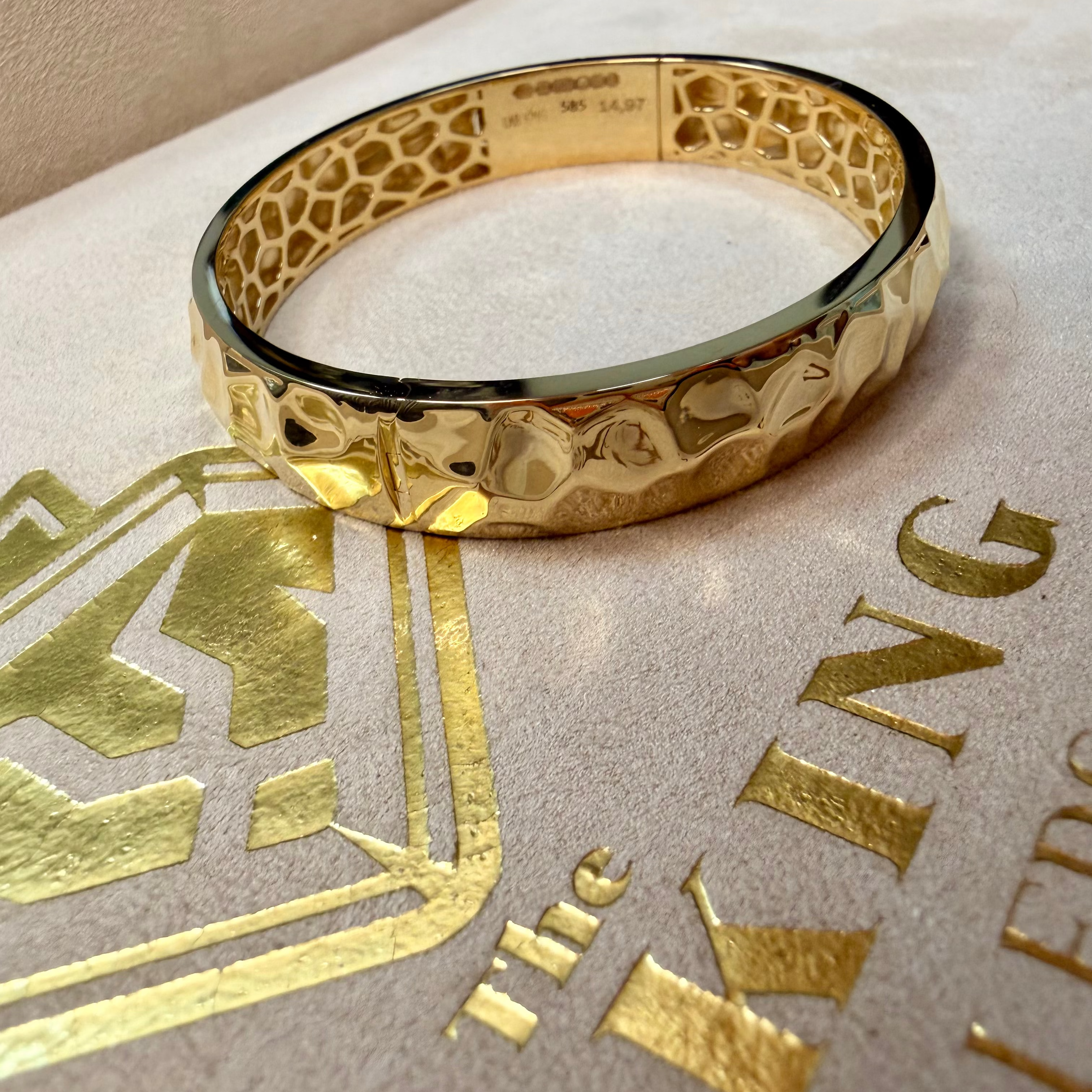 Gold bracelet on a textured surface with 'The King's' branding.