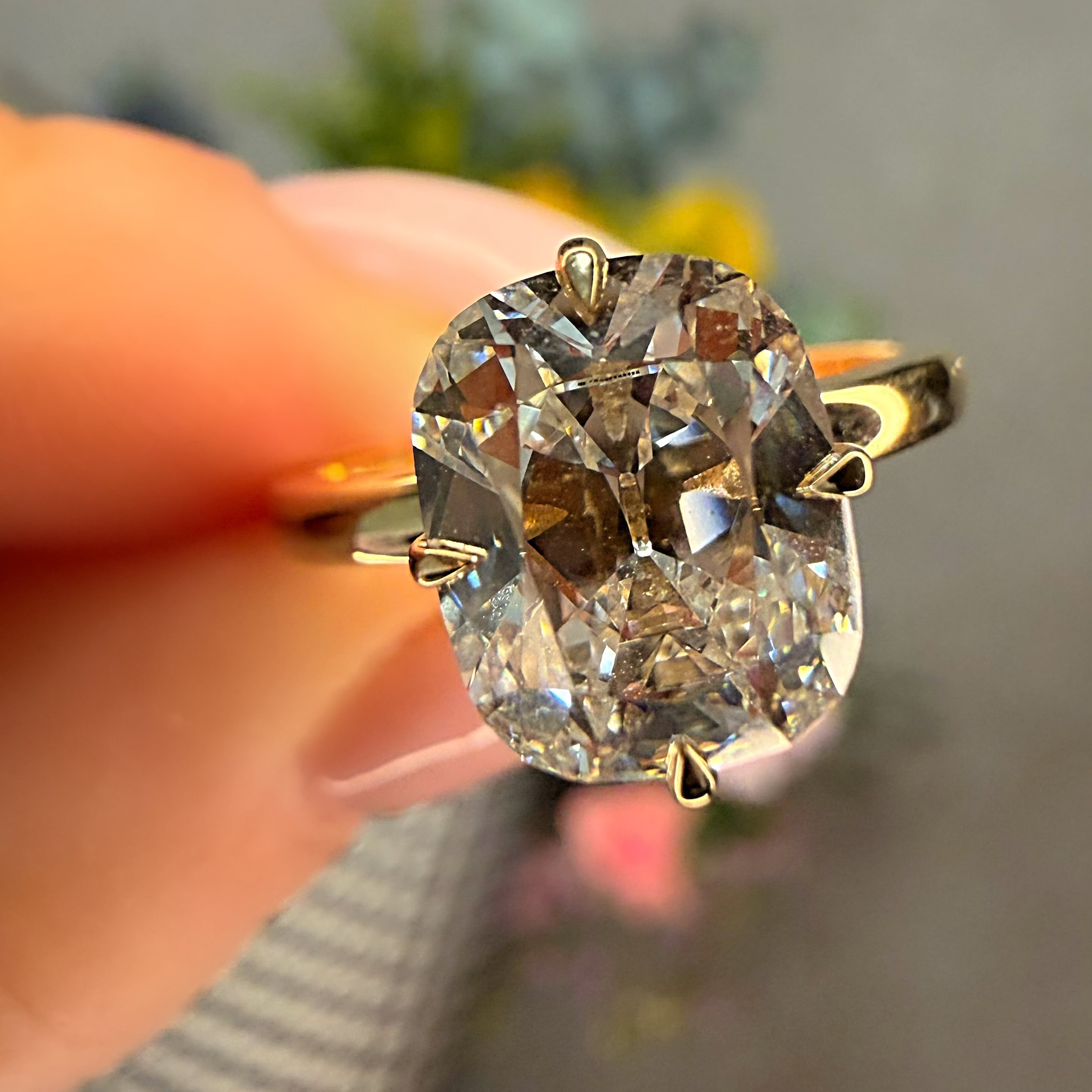 Gold ring with a large diamond held by a hand against a blurred background