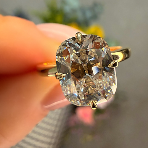 Gold ring with a large diamond held by a hand against a blurred background