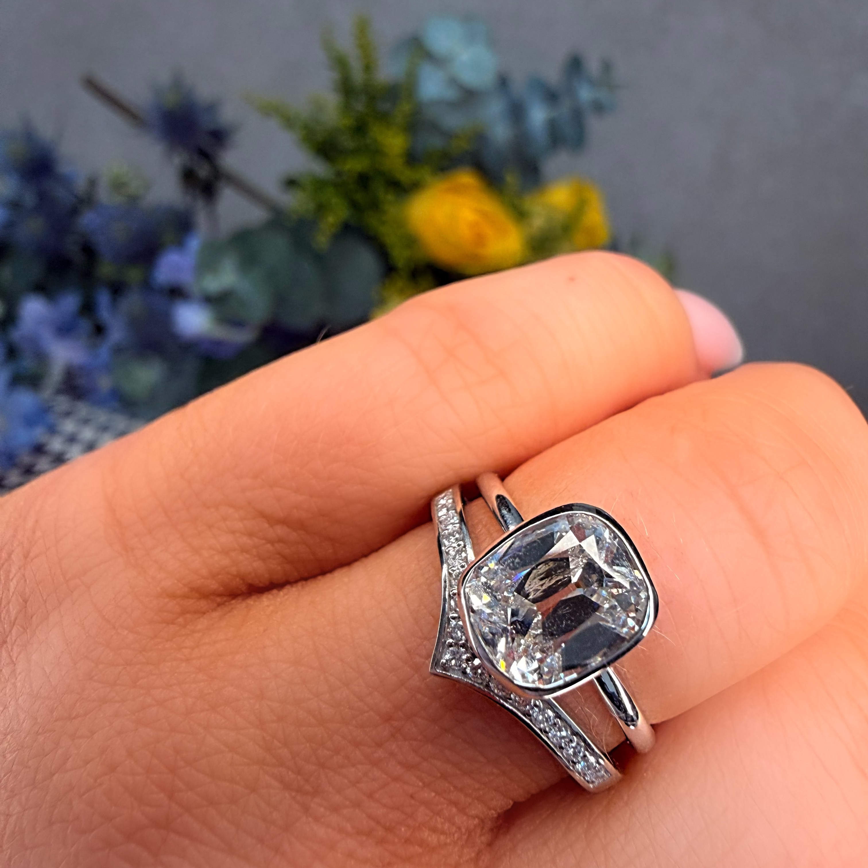 Silver ring with a large gemstone on a hand, blurred flowers in the background