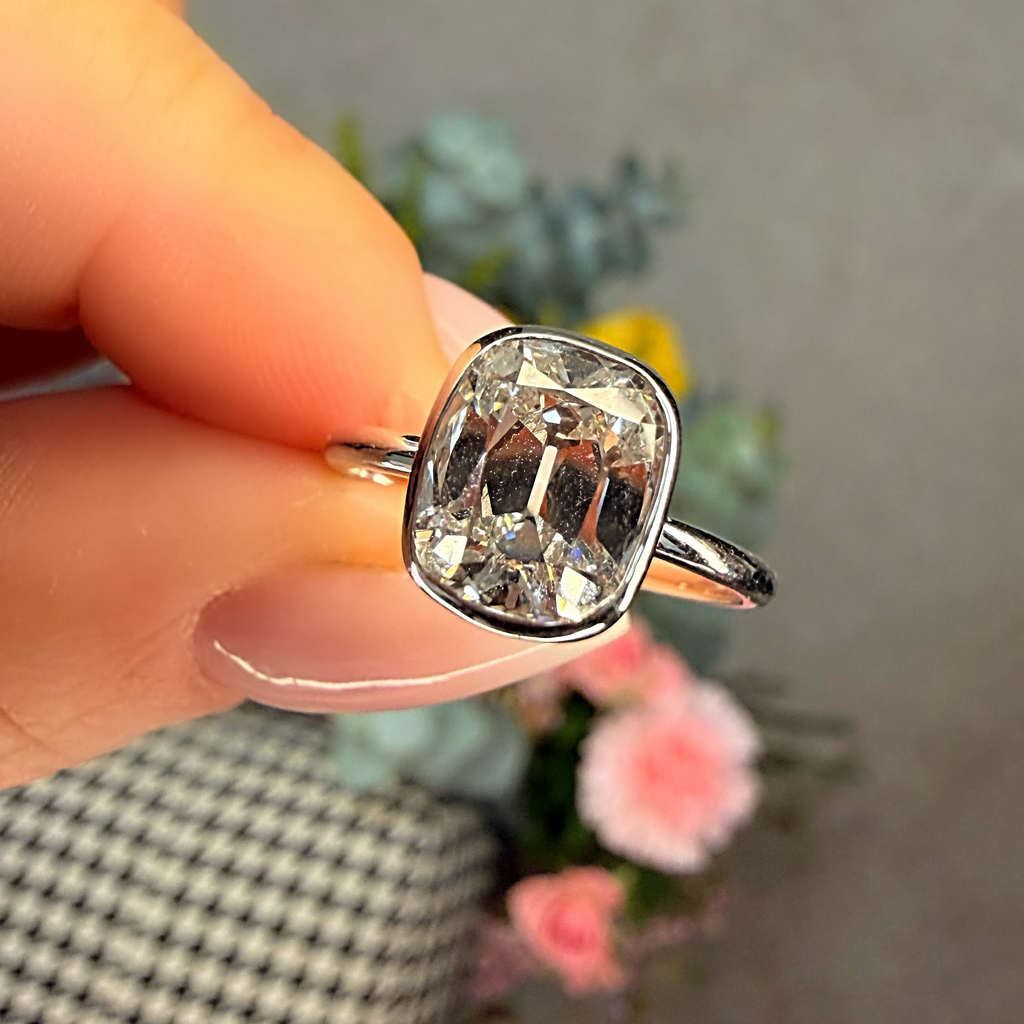Silver ring with a large diamond held by a hand against a blurred background