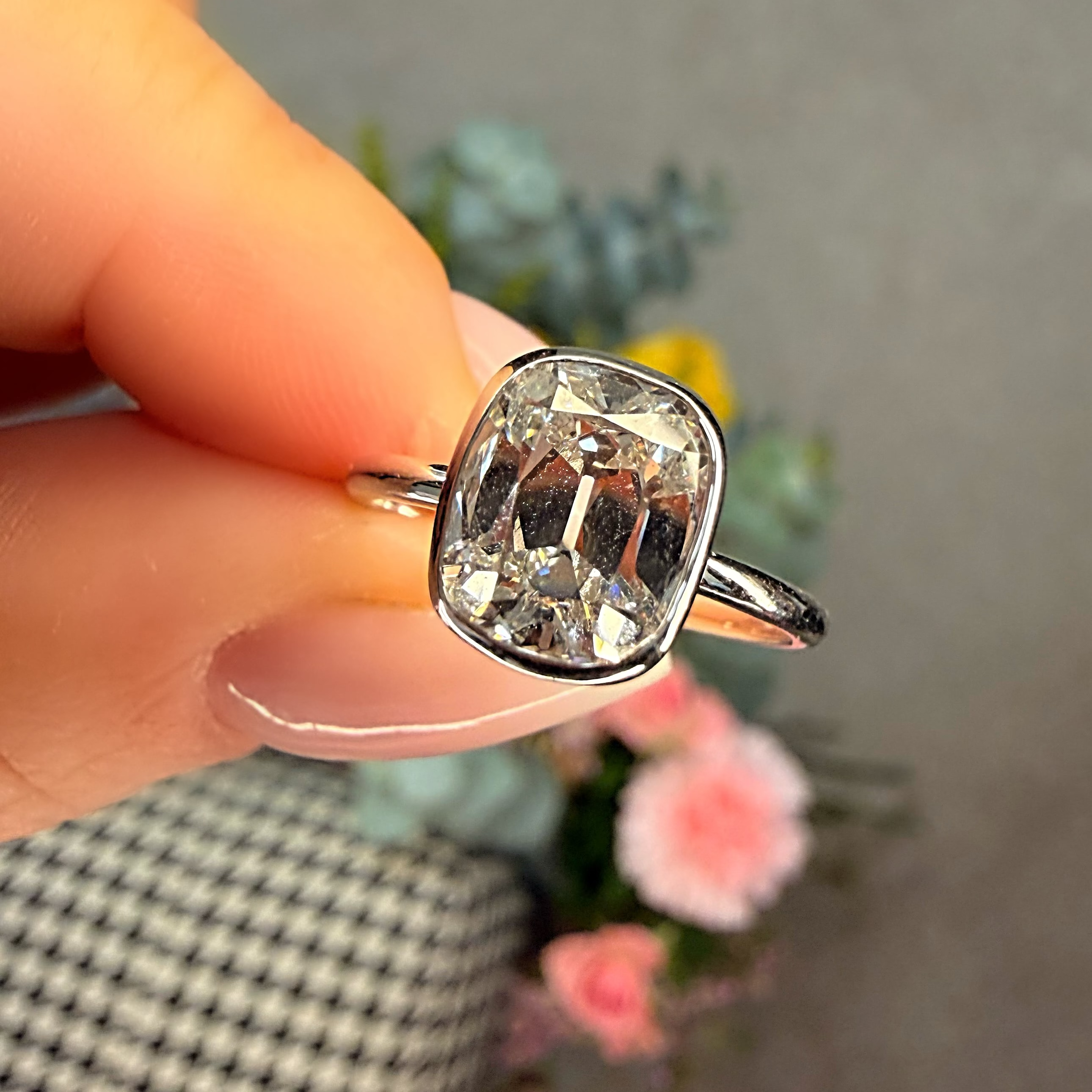 Silver ring with a large diamond held by a hand against a blurred background