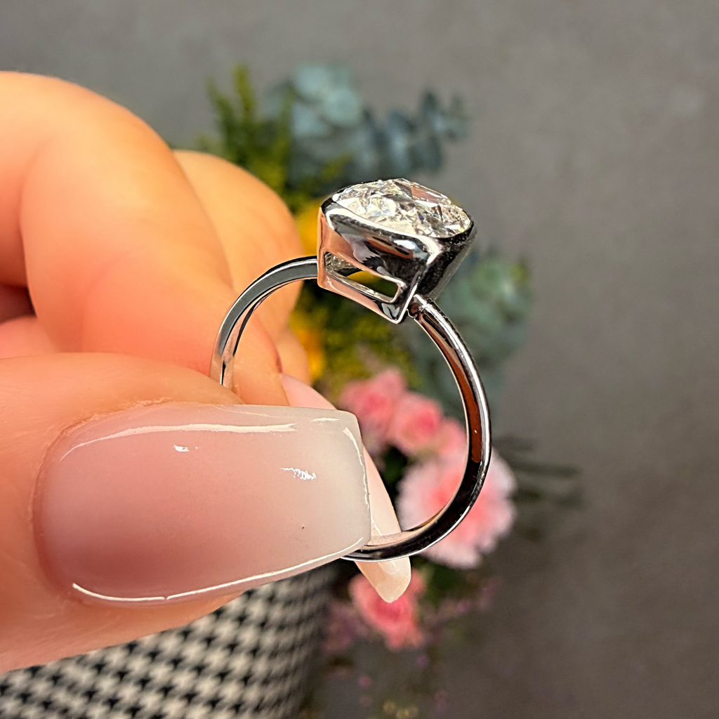 Diamond ring held by a hand with a blurred floral background