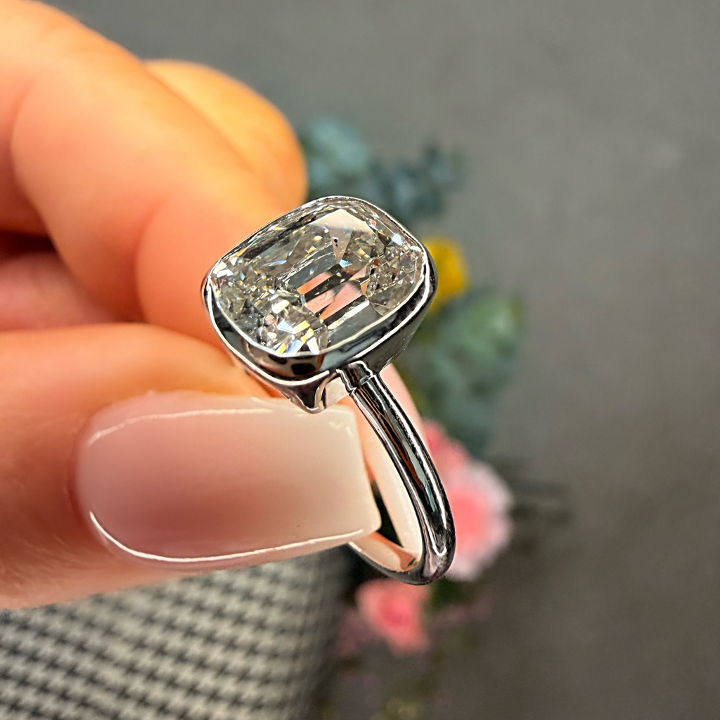 Silver ring with a large diamond held by a hand against a blurred background