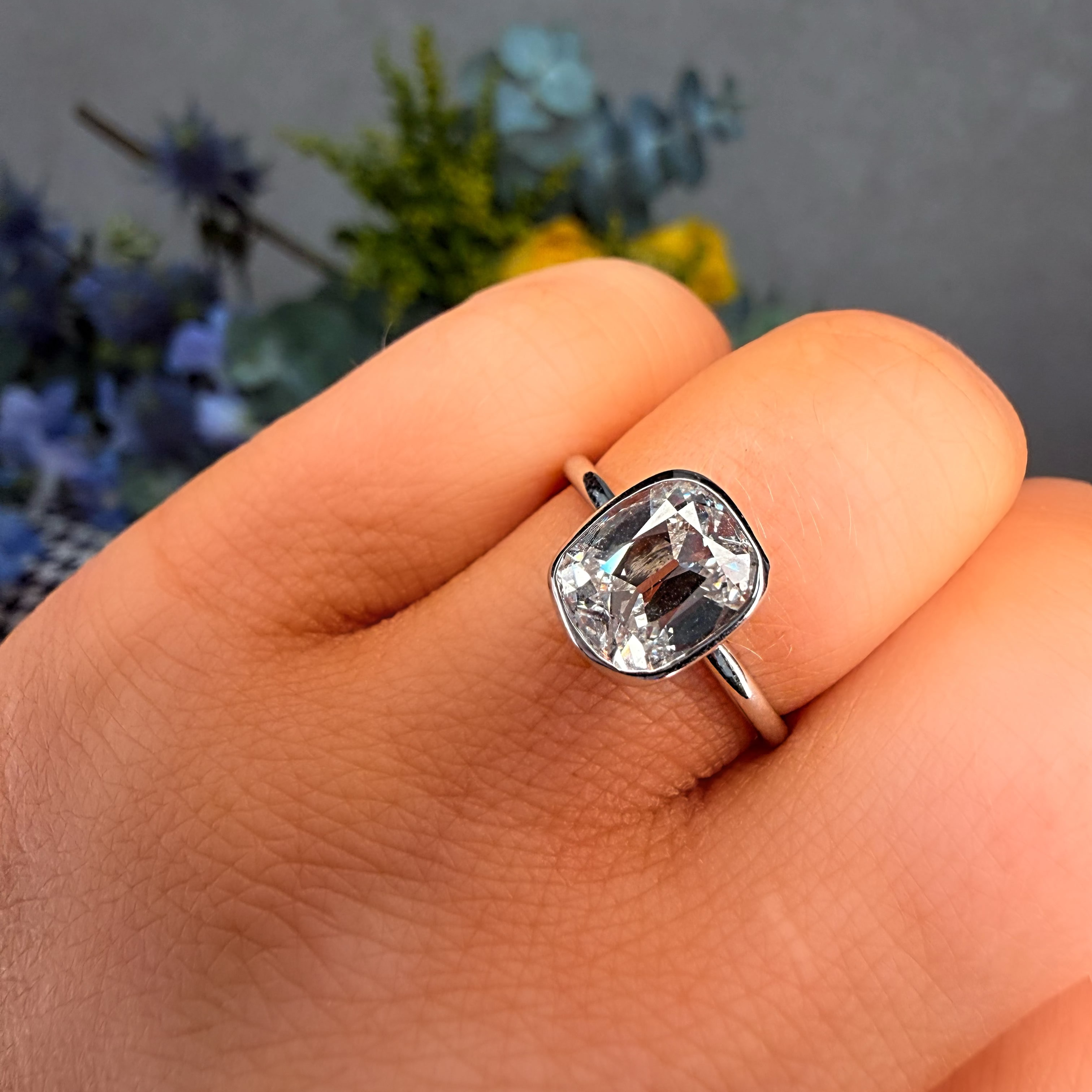 Silver ring with a large diamond on a finger against a blurred floral background
