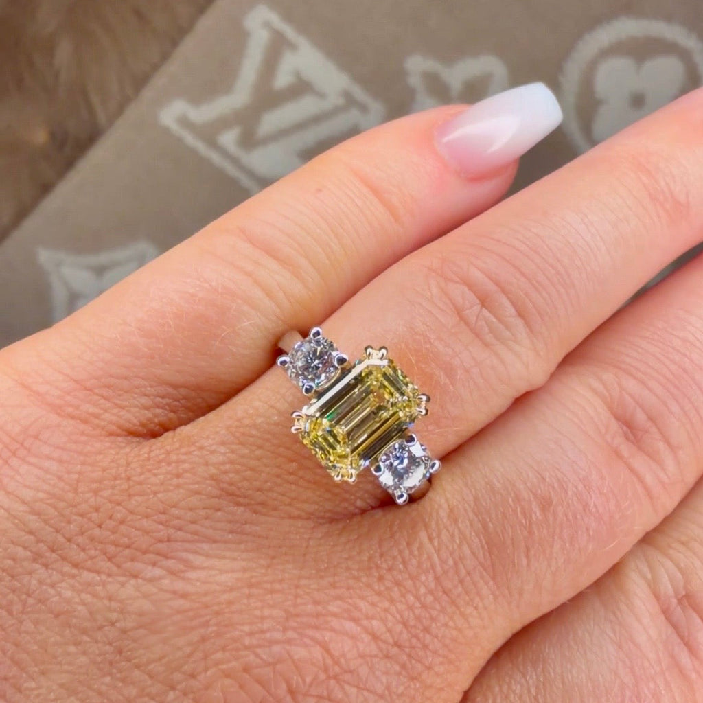 Ring with a yellow gemstone and smaller diamonds on a hand, with a patterned background.