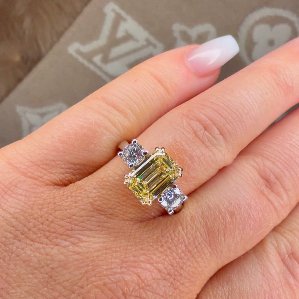 Ring with a yellow gemstone and smaller diamonds on a hand, with a patterned background.