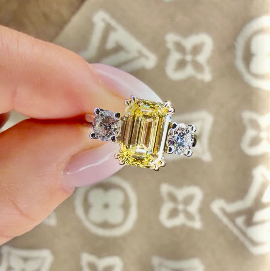 Yellow diamond ring held by a hand on a patterned fabric background