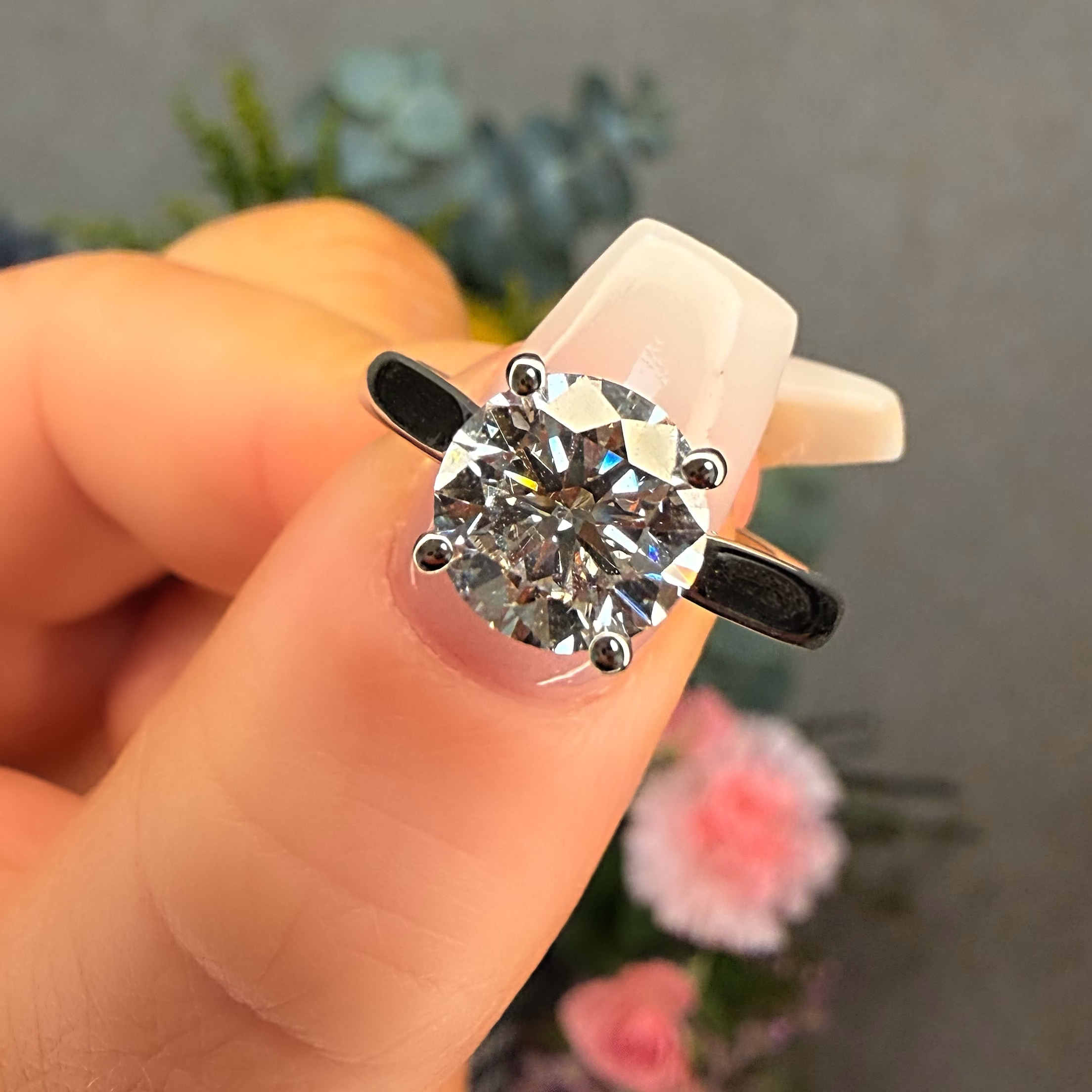 Diamond ring held in a hand with a blurred floral background