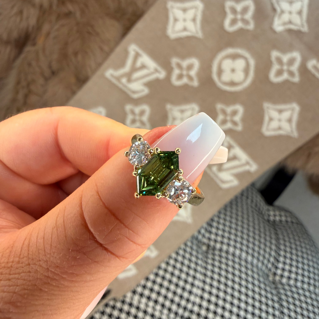 Hand holding a ring with green gemstone and clear stones against a patterned background