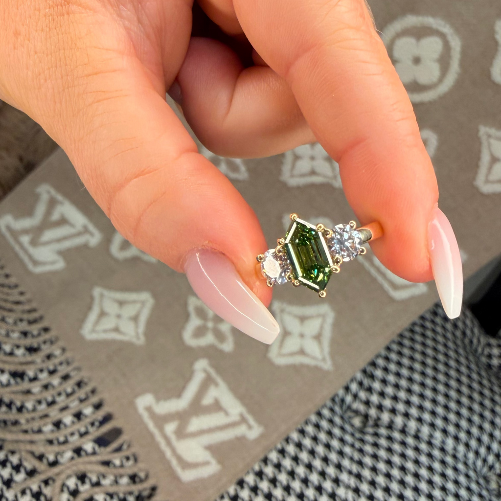 Hand holding a green gemstone ring on a patterned surface