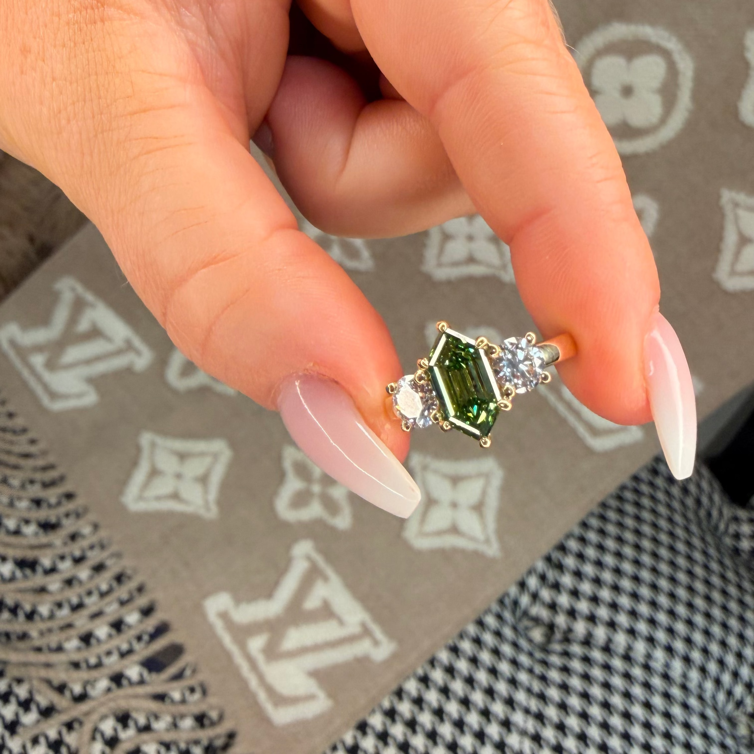 Hand holding a green gemstone ring on a patterned surface