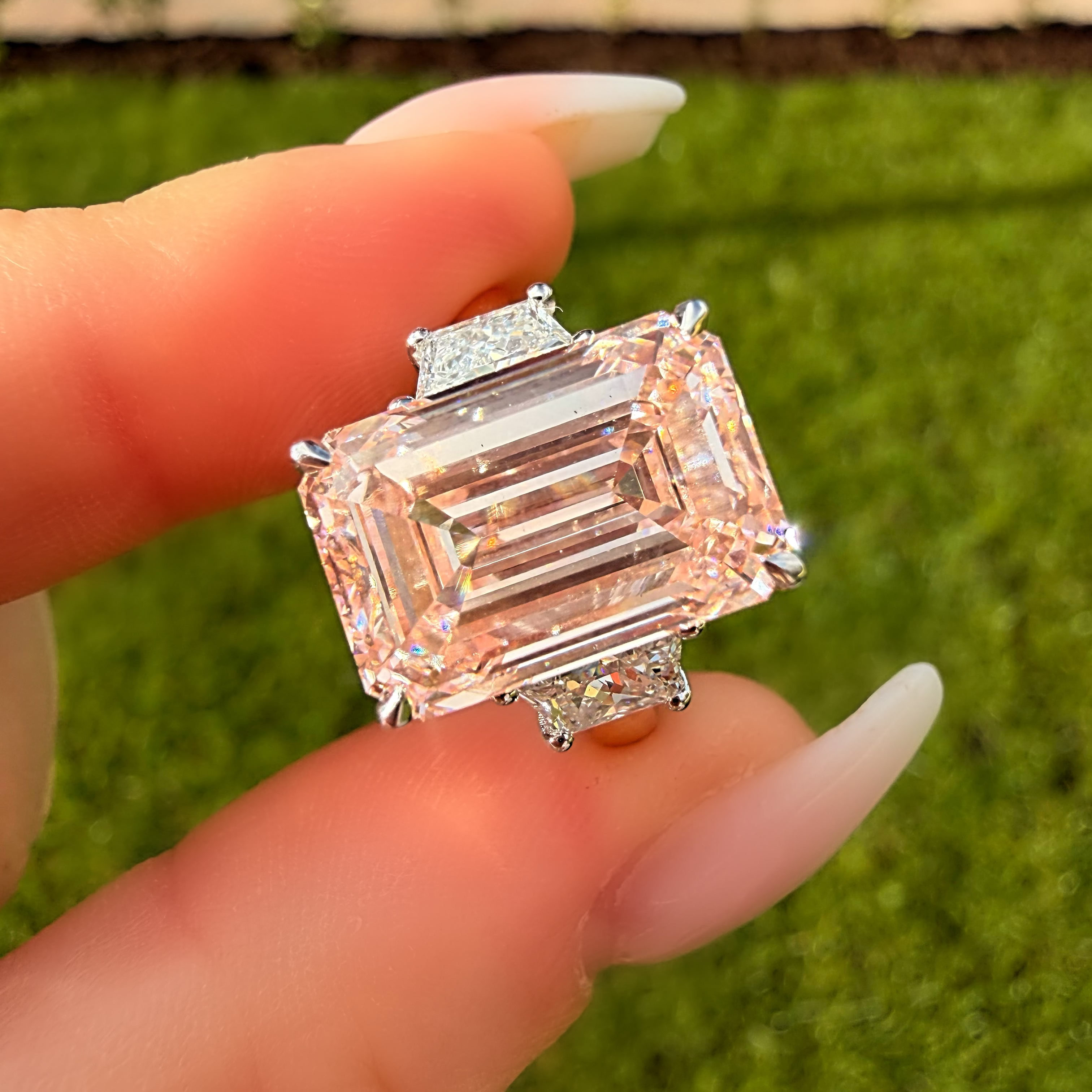 Diamond ring held by a hand with a blurred green background