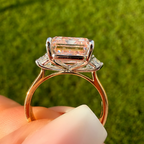 Rose gold ring with a large diamond held against a green leaf background