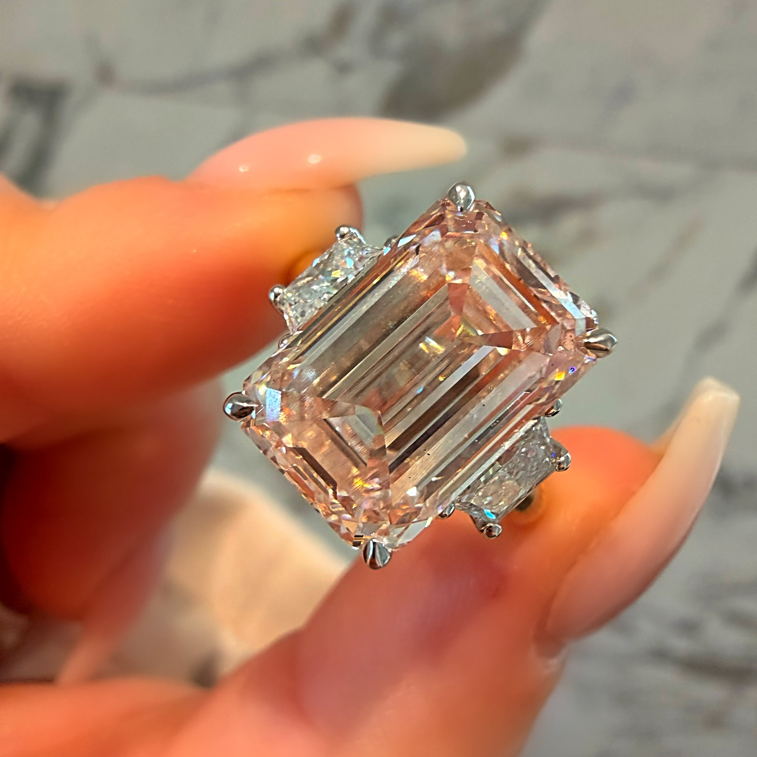 Diamond ring held by a hand against a marble background