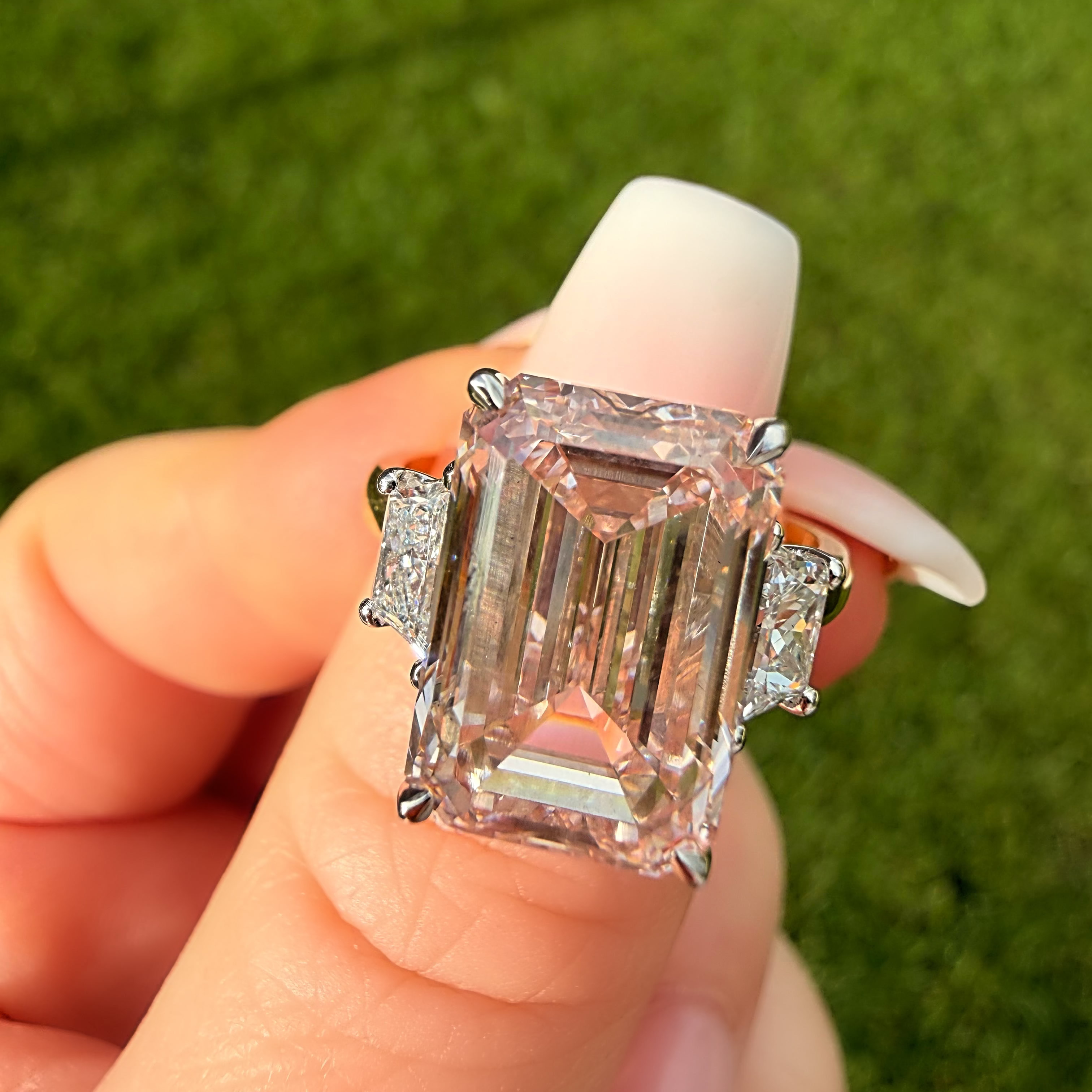 Ring with a large pink diamond held by a hand against a green grass background