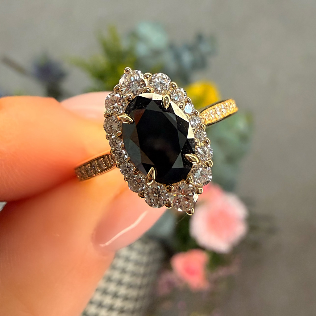 Gold ring with a black gemstone held by a hand against a blurred floral background
