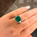 Hand wearing a ring with a green gemstone on a patterned surface