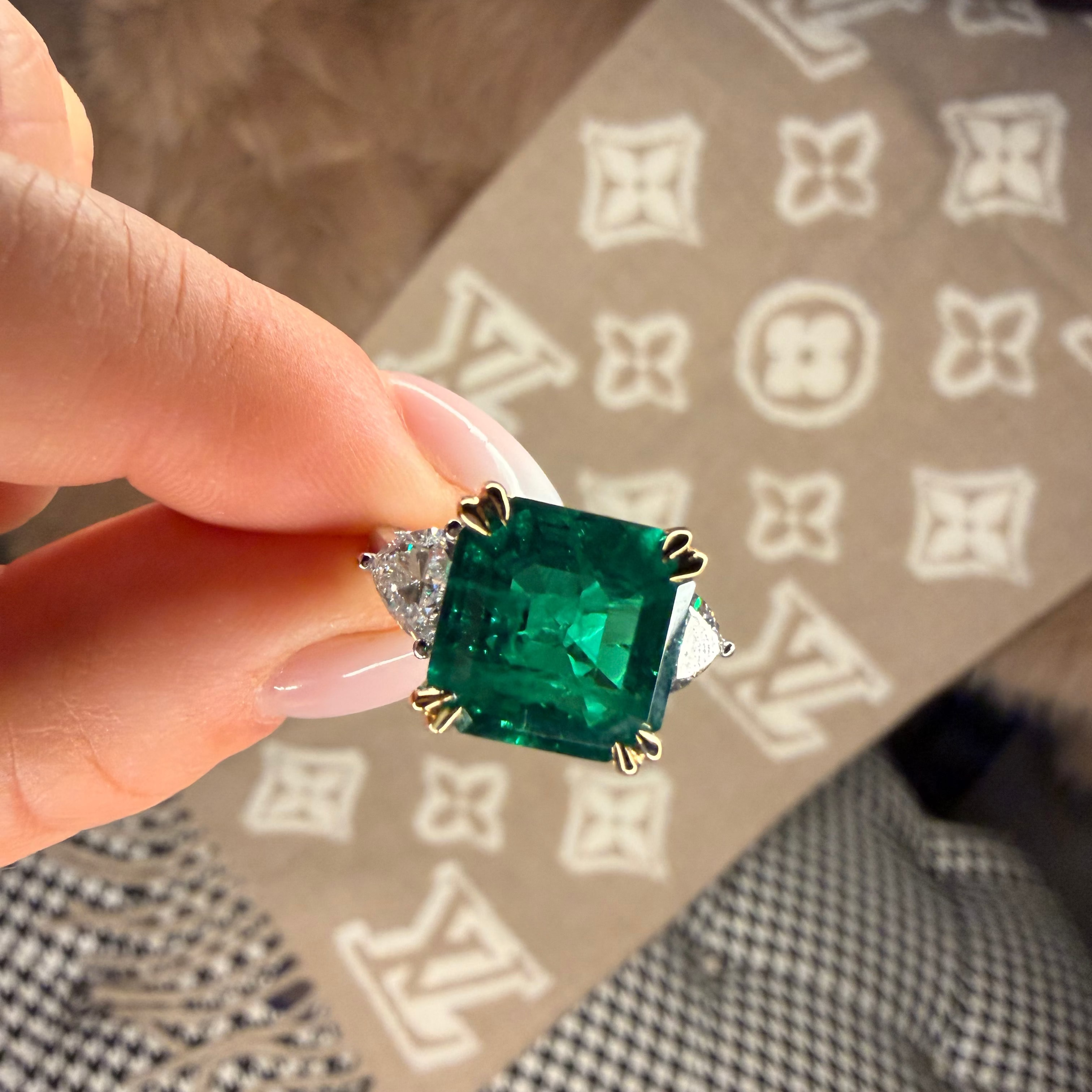 Emerald green gemstone ring held by a hand on a patterned surface