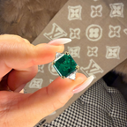 Green gemstone earring held by a hand with a patterned surface in the background